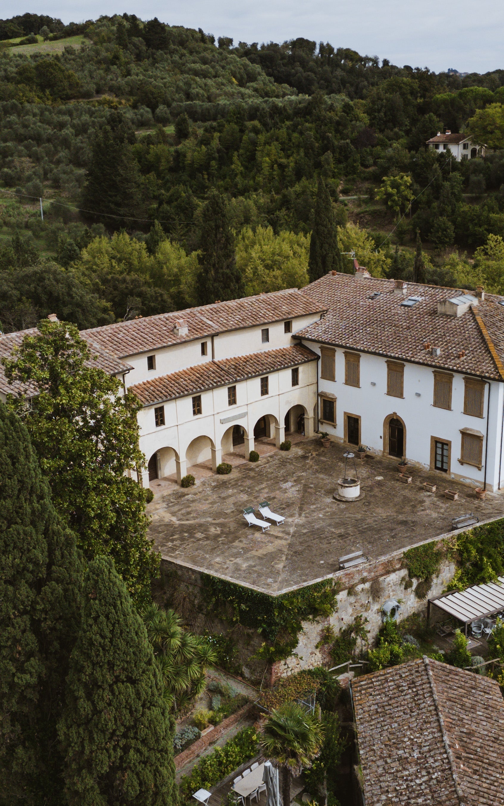 Tuscan countryside villa with stone courtyard and sun loungers surrounded by lush greenery